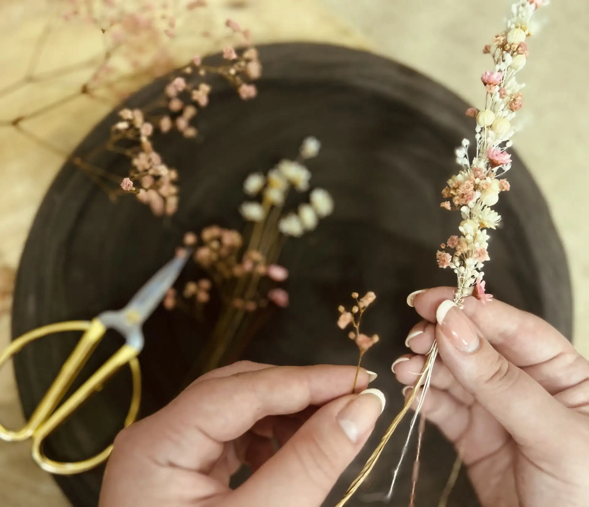 Photo de mains réalisant une couronne de fleurs séchées